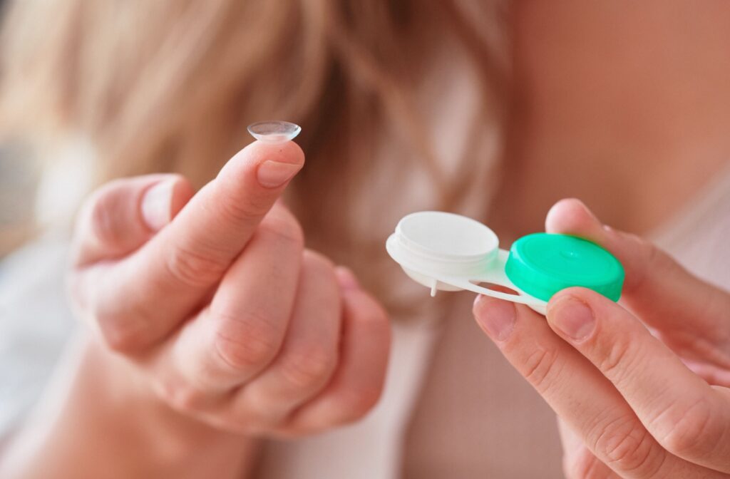 A contact lens rests on a pointer finger while the other hand holds the lens case.
