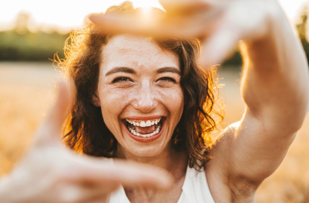 A person outside in the sun, smiling, framing her face by making a square with pointer finger and thumb on each hand