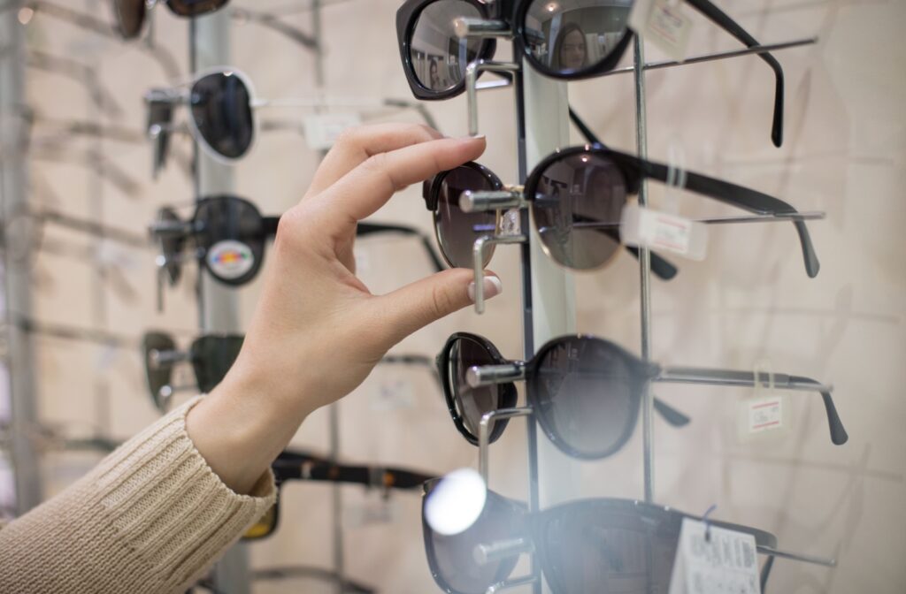 A hand grabbing a pair of sunglasses off a display shelf in an optometry office.