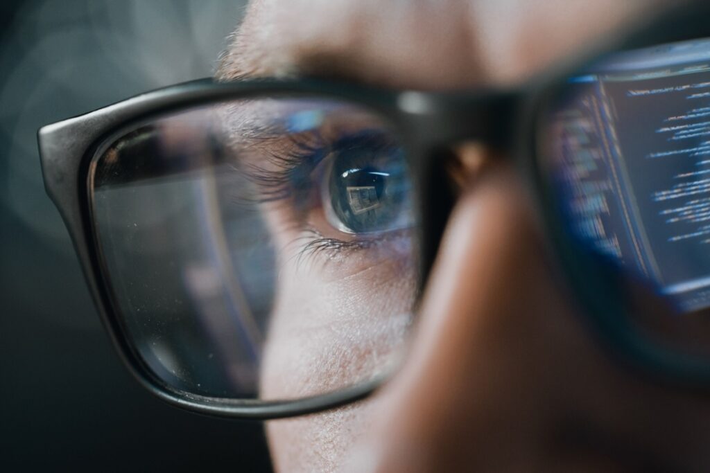 A close up of a person wearing blue light protective glasses while staring at a computer screen at work.